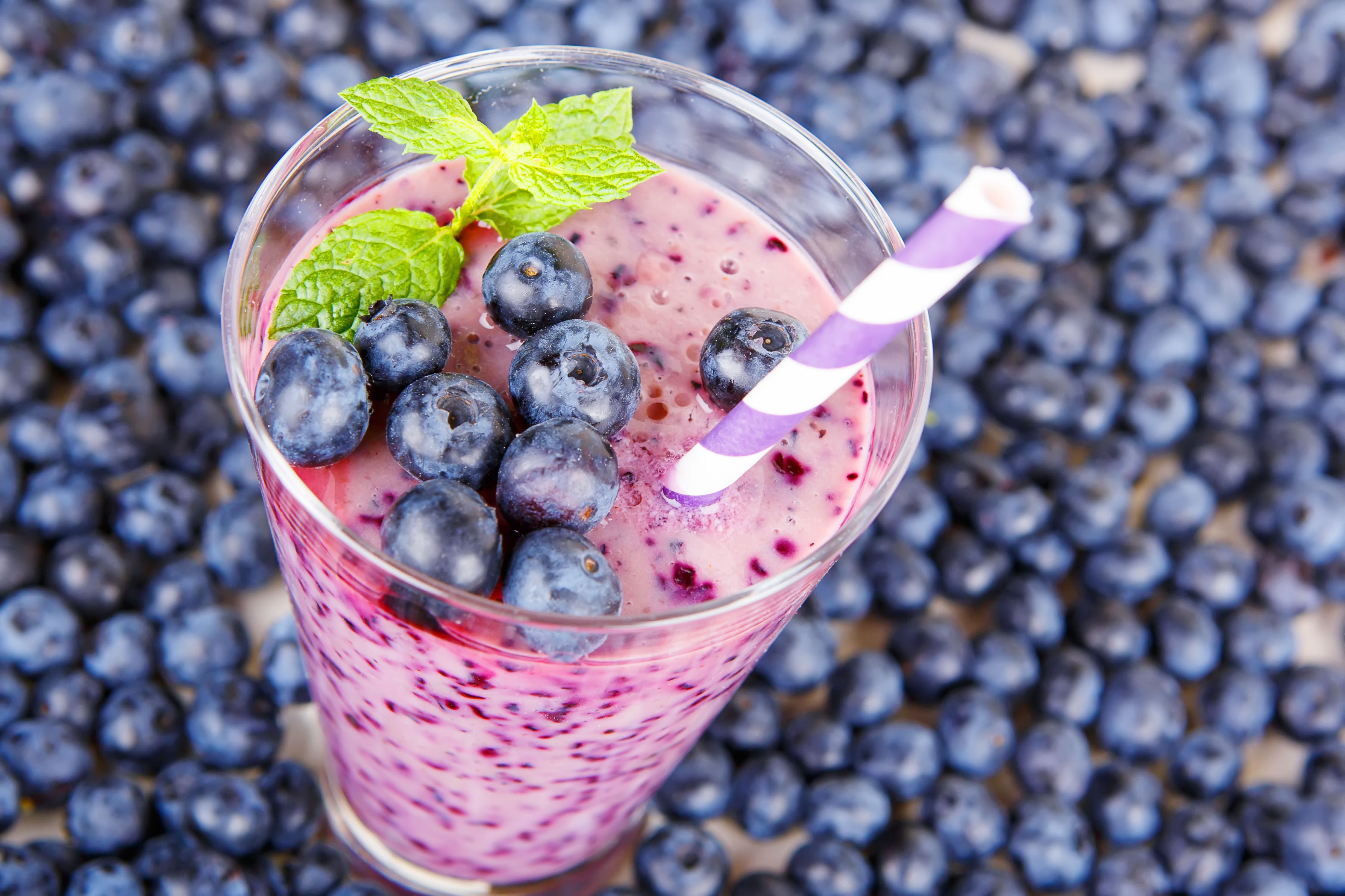 Blueberry smoothie in a glass jar with a straw and sprig of mint